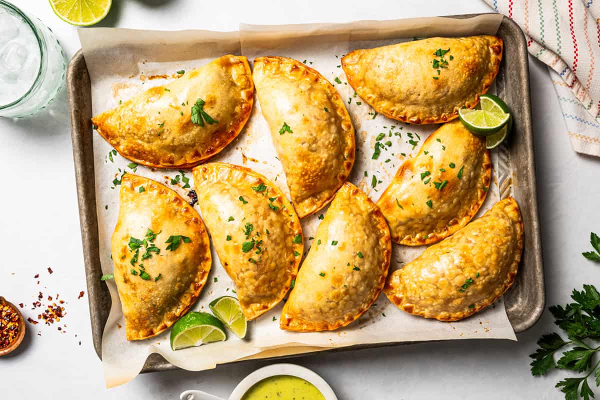 Chicken empanadas arranged on a baking sheet.