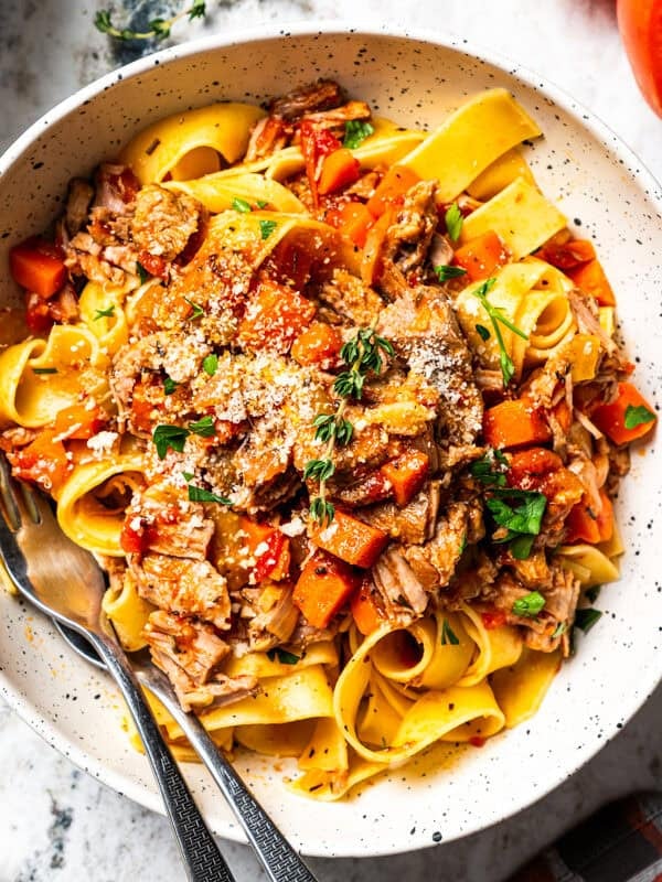 A bowl of pork ragu with pappardelle pasta served with toasted bread on the side and garnished with Parmesan cheese.