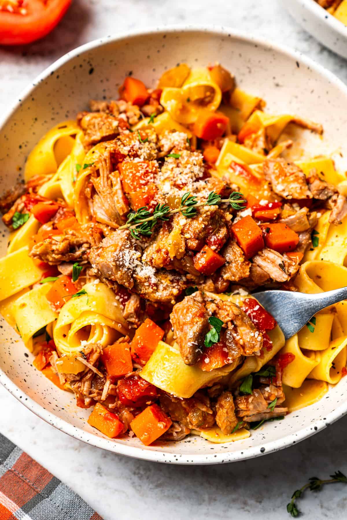 This slow-braised pork ragu recipe cooks for hours in the oven until fall-apart tender and ready to shred into a rich, flavorful meat sauce. A bowl of pappardelle tossed with homemade pork ragu, garnished with Parmesan and fresh thyme.