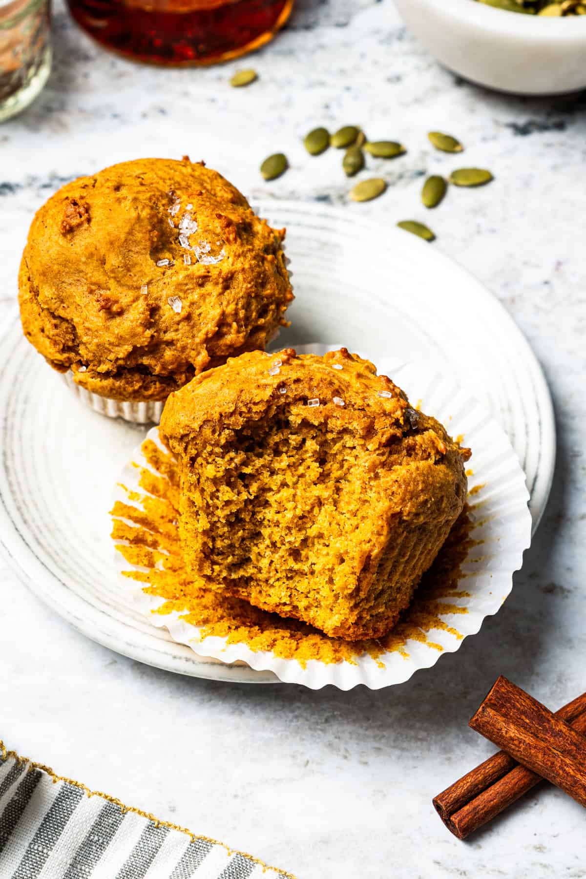 Moist, fluffy pumpkin protein muffins are a high-protein fall treat made with vanilla whey powder, Greek yogurt, eggs, and pumpkin purée. Pumpkin protein muffins on a plate, including one broken open to show the soft pumpkin center.