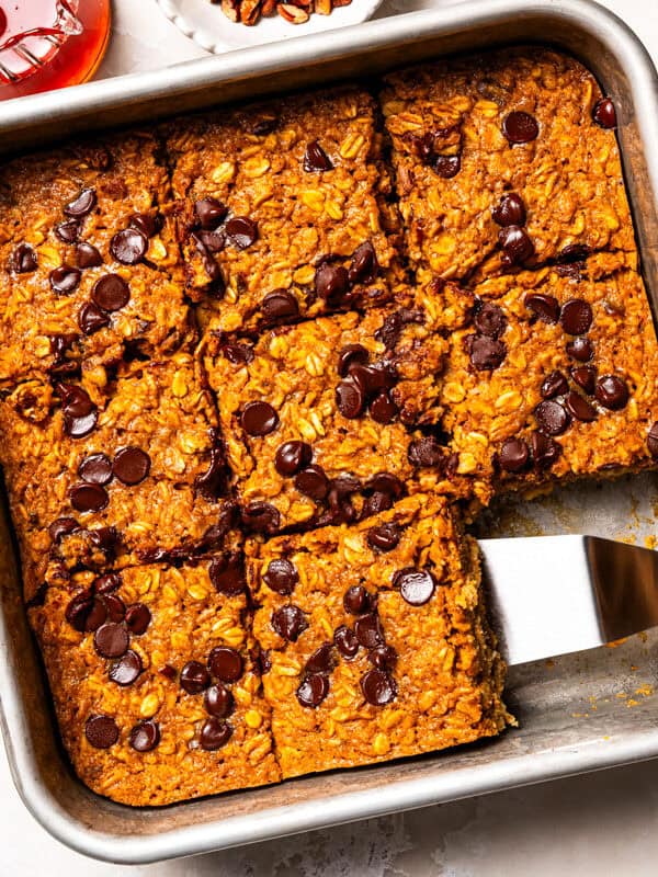 Pumpkin baked oatmeal in a baking dish, with a server popping out a slice.