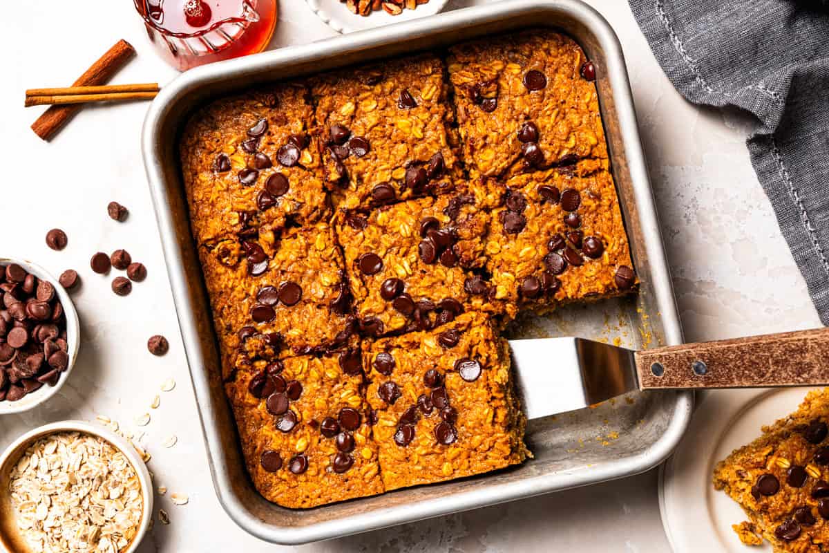 Pumpkin baked oatmeal is the perfect easy, make-ahead fall breakfast! Filled with hearty oats, warm spices, pumpkin purée, and maple syrup. Pumpkin baked oatmeal in a baking dish, with a server popping out a slice.