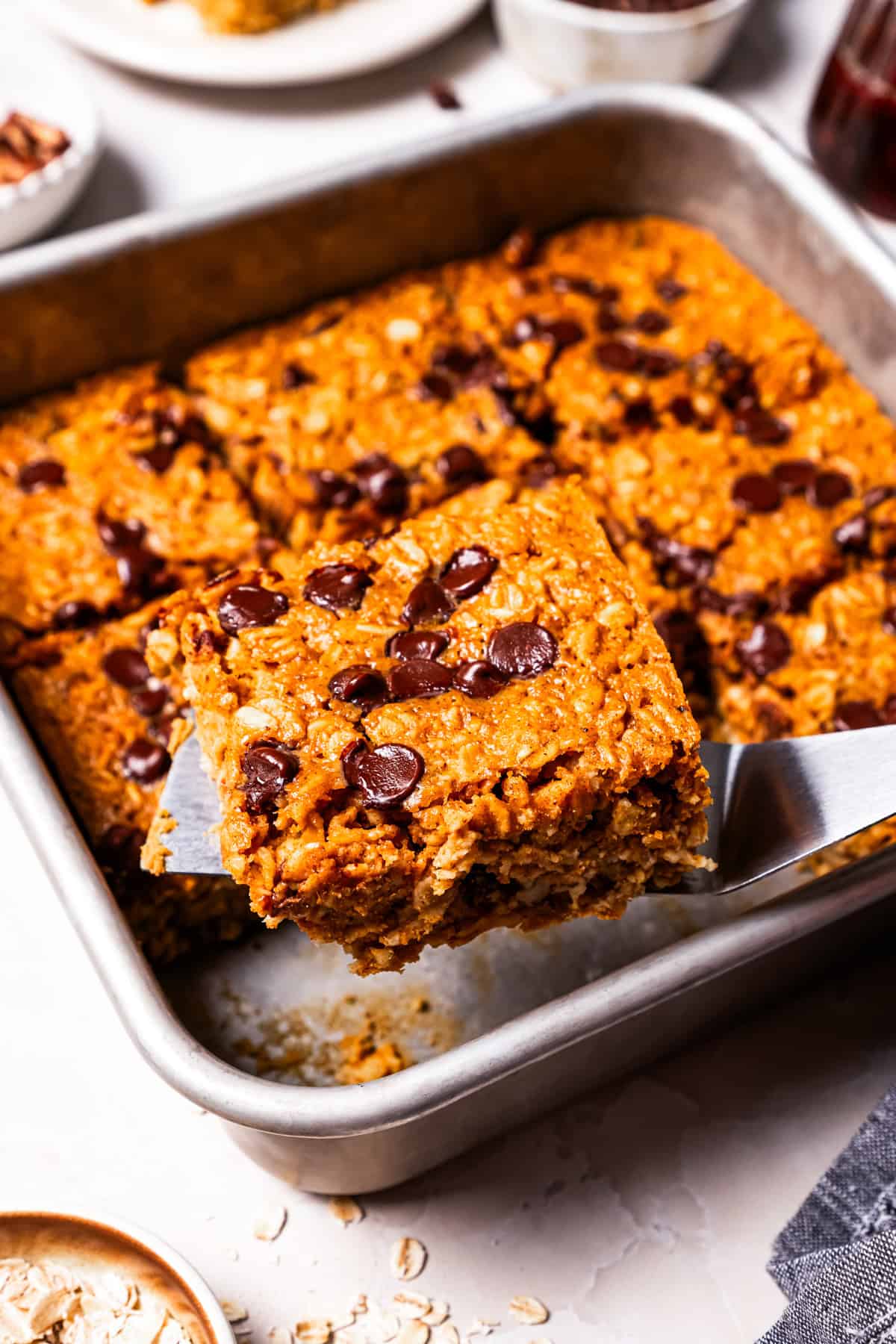 Pumpkin baked oatmeal is the perfect easy, make-ahead fall breakfast! Filled with hearty oats, warm spices, pumpkin purée, and maple syrup. Spatula lifting a slice of pumpkin baked oatmeal.