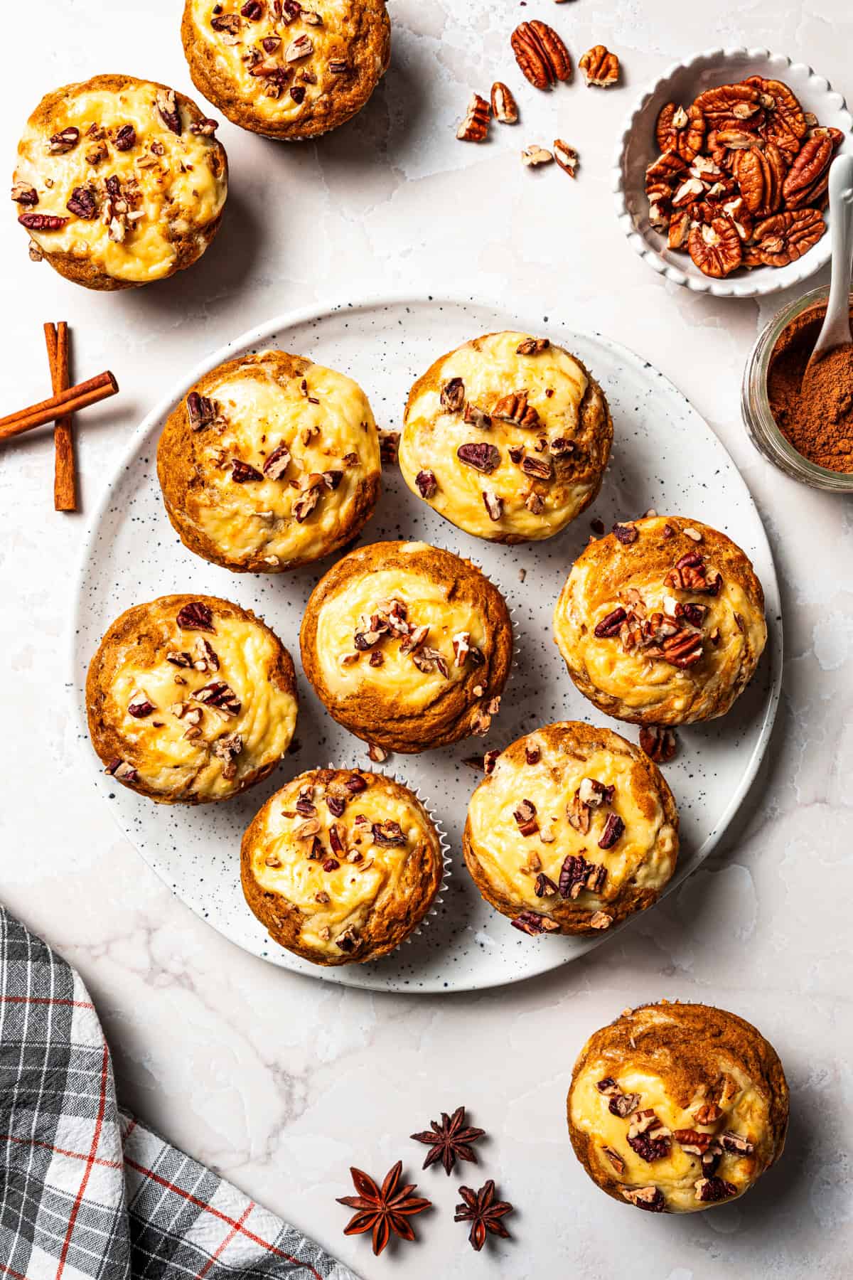 These pumpkin cream cheese muffins are moist, spiced pumpkin muffins swirled with cream cheese filling and topped with toasted pecans. Pumpkin muffins with cream cheese, topped with chopped pecans and arranged on a plate.
