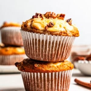 Two pumpkin cream cheese muffins stacked on a countertop.