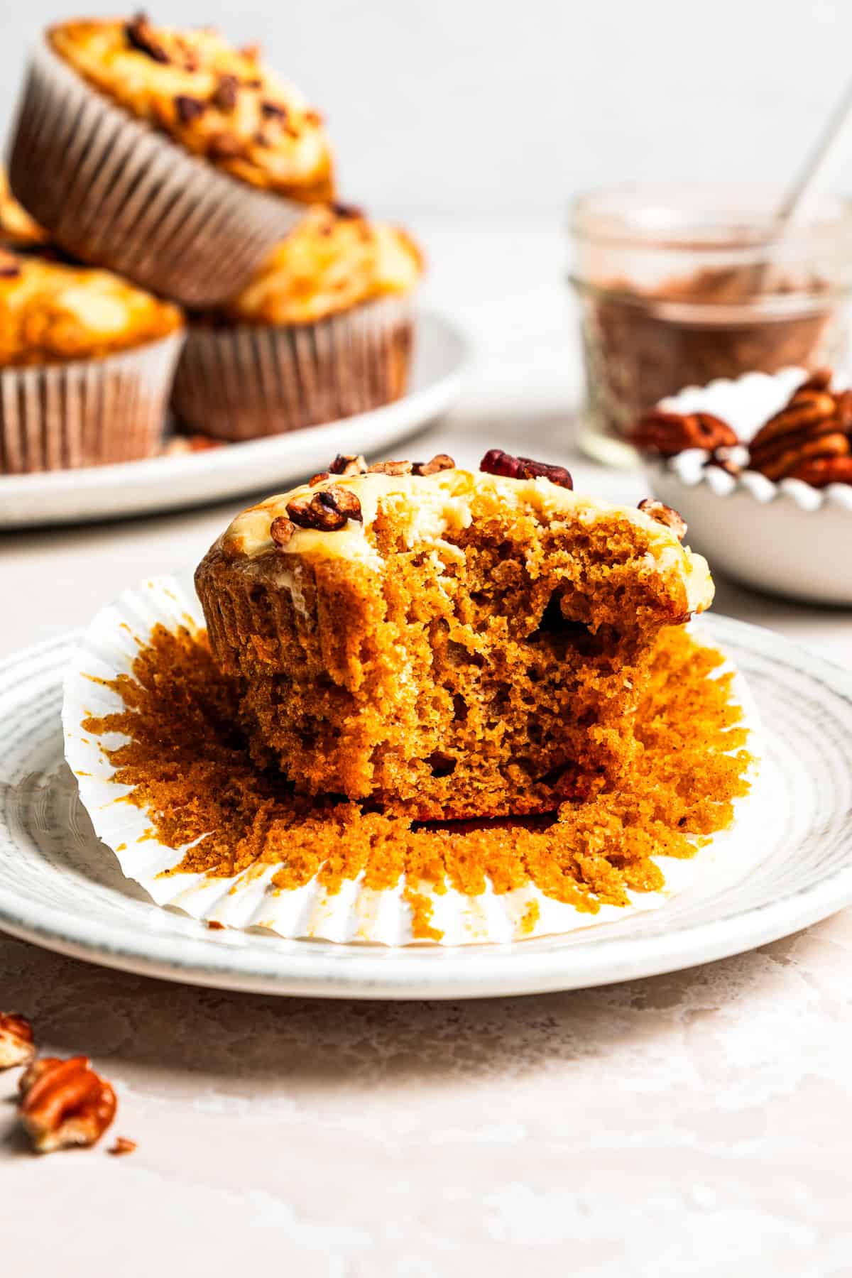 These pumpkin cream cheese muffins are moist, spiced pumpkin muffins swirled with cream cheese filling and topped with toasted pecans. Pumpkin cream cheese muffin broken open to show the moist pumpkin crumb.