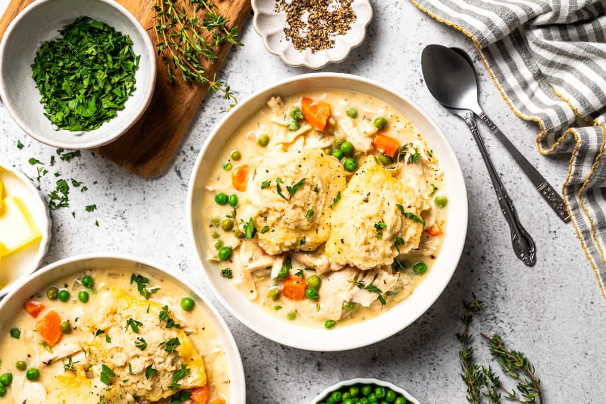 This slow cooker chicken and dumplings recipe is a cozy, creamy chicken stew loaded with homemade biscuit dumplings. All cooked in one pot! Slow cooker chicken and dumplings served in bowls with tender chicken, carrots, peas, and fluffy homemade dumplings.