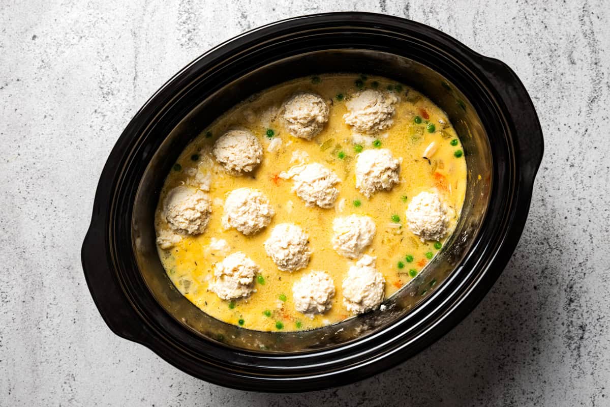 This slow cooker chicken and dumplings recipe is a cozy, creamy chicken stew loaded with homemade biscuit dumplings. All cooked in one pot! Scoops of dumpling dough added over the chicken and vegetable filling in a slow cooker.