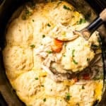 Slow cooker chicken and dumplings in a slow cooker with a spoon scooping up chicken, vegetables, and dumplings.