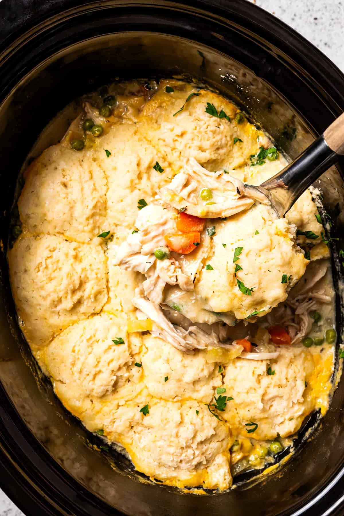 This slow cooker chicken and dumplings recipe is a cozy, creamy chicken stew loaded with homemade biscuit dumplings. All cooked in one pot! Slow cooker chicken and dumplings in a slow cooker with a spoon scooping up chicken, vegetables, and dumplings.