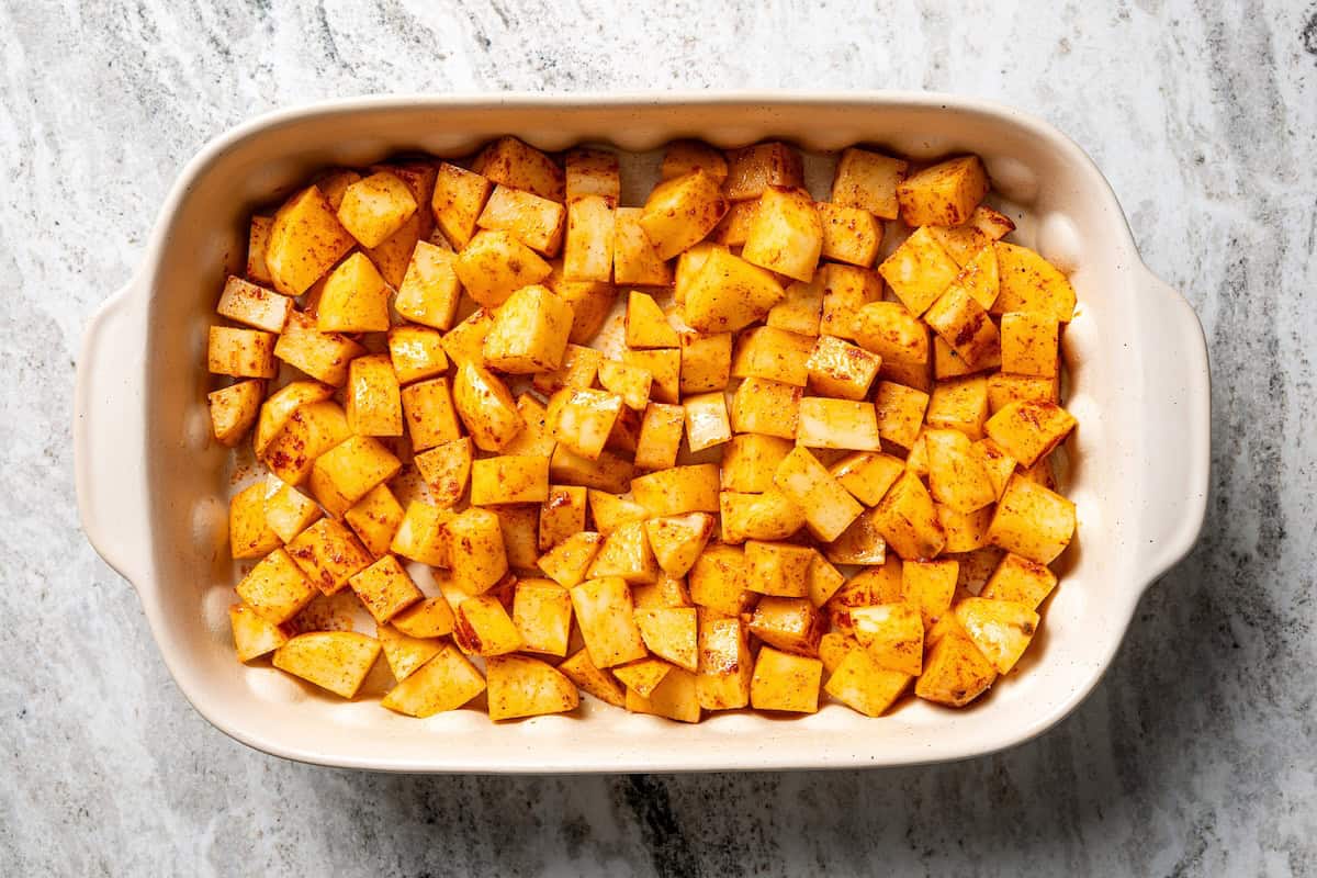 This chicken potato casserole combines juicy seasoned chicken and potatoes, baked in one pan and loaded with bacon, cheese, and sour cream. Seasoned potatoes spread into a casserole dish.