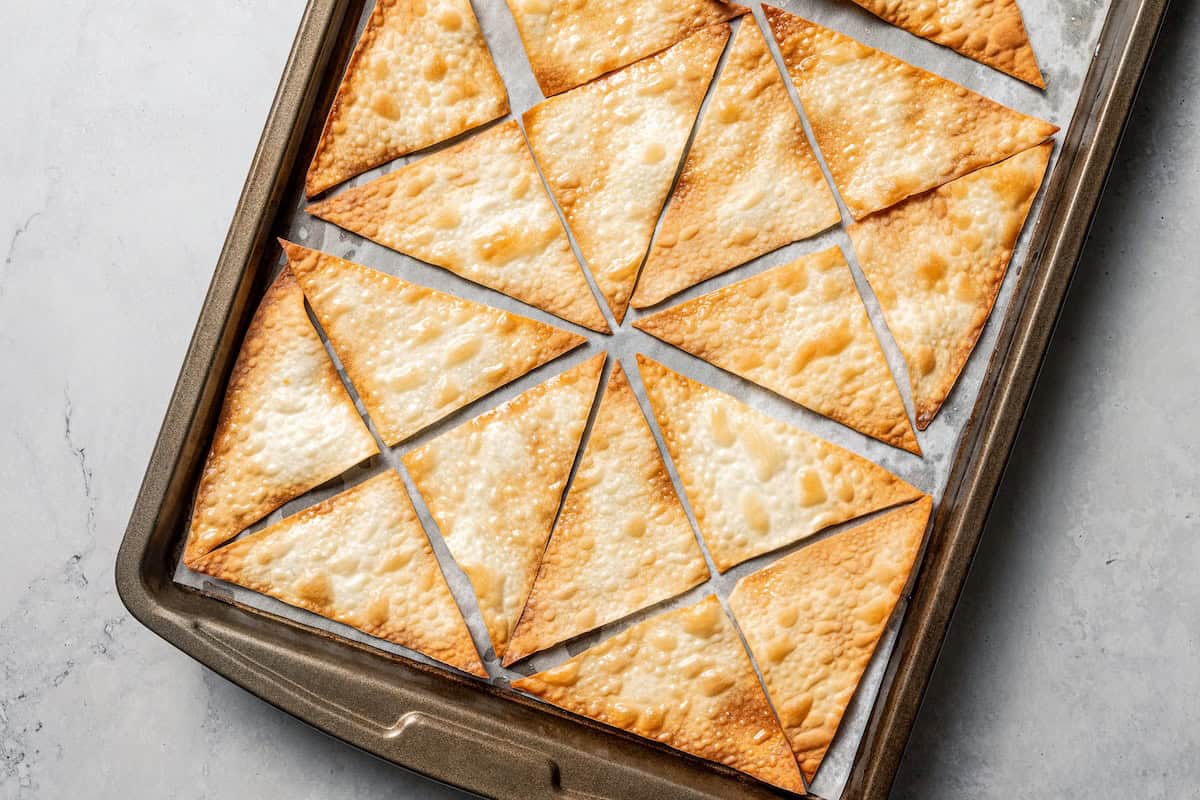 Crab rangoon dip has all those creamy flavors in an easy baked crab dip with cream cheese, sweet chili, green onion, and crispy wonton chips. Golden-baked wonton chips on a lined baking sheet.