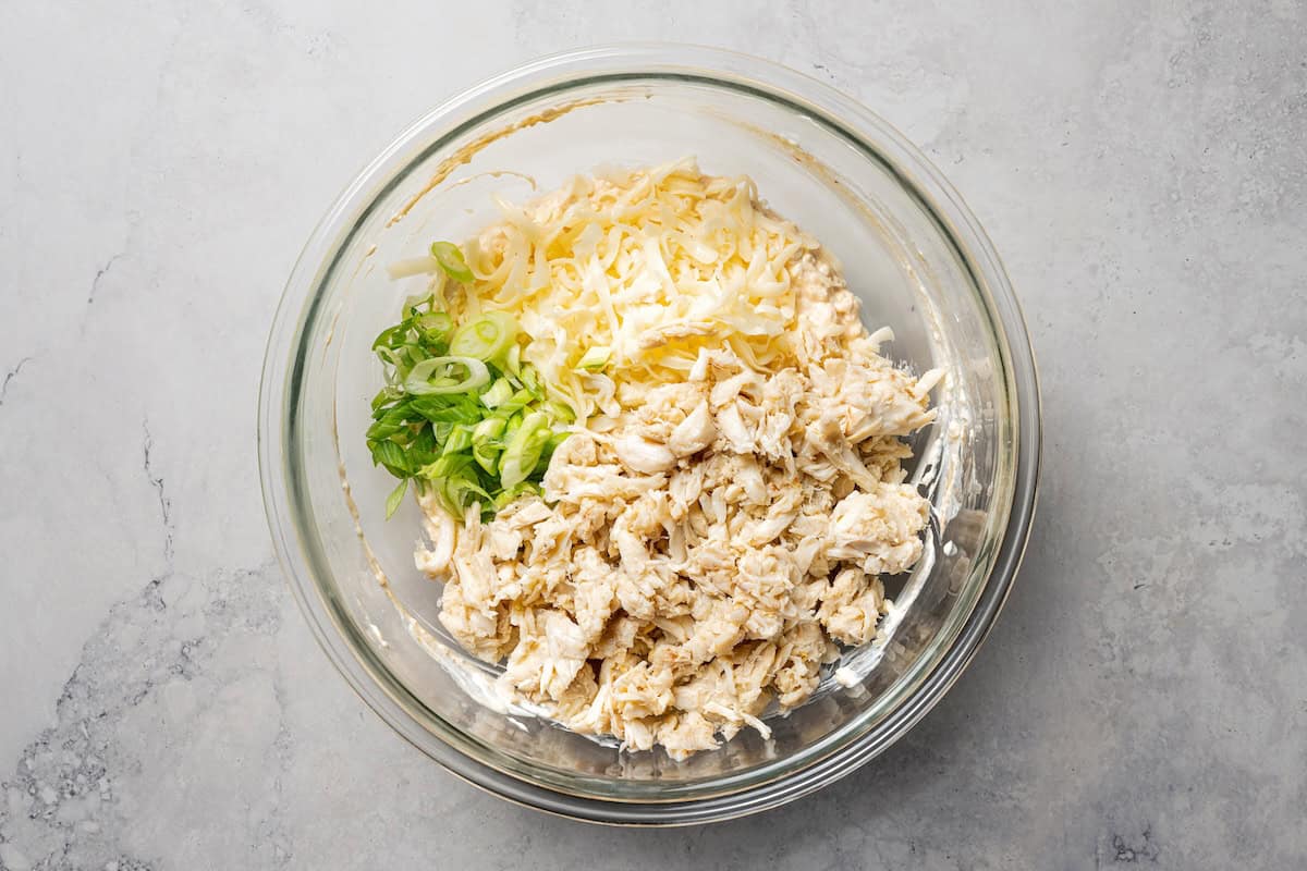 Crab rangoon dip has all those creamy flavors in an easy baked crab dip with cream cheese, sweet chili, green onion, and crispy wonton chips. Lump crab and shredded cheese added to crab rangoon dip ingredients in a bowl.