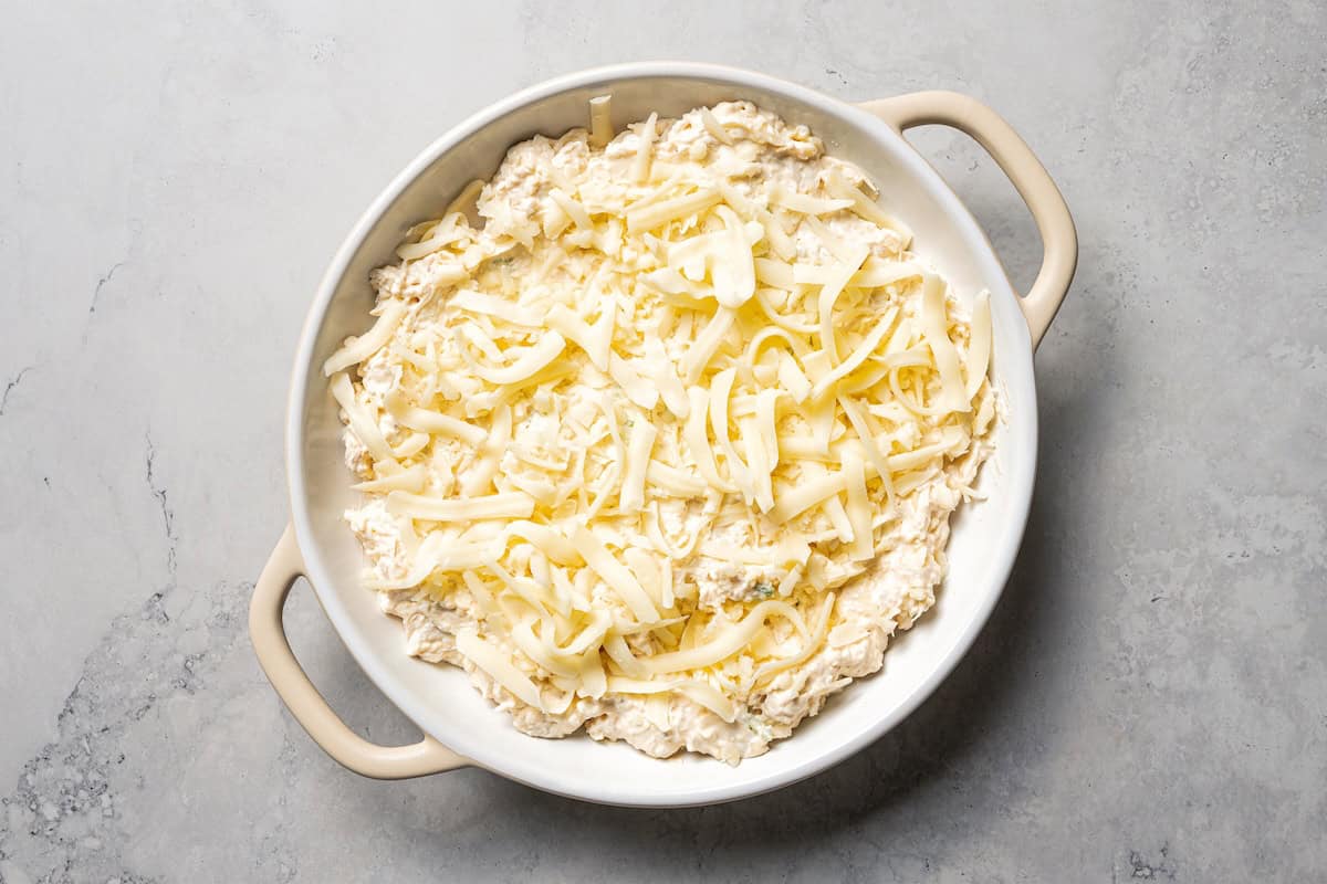 Crab rangoon dip has all those creamy flavors in an easy baked crab dip with cream cheese, sweet chili, green onion, and crispy wonton chips. Shredded cheese sprinkled on top of crab rangoon dip in a baking dish.