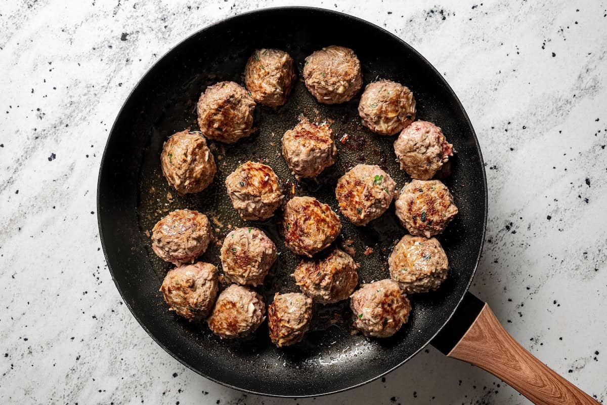Not your old-fashioned porcupine meatballs! Make these with juicy ground beef, sausage, rice, and herbs, cooked in homemade tomato sauce. Browned porcupine meatballs in a skillet.