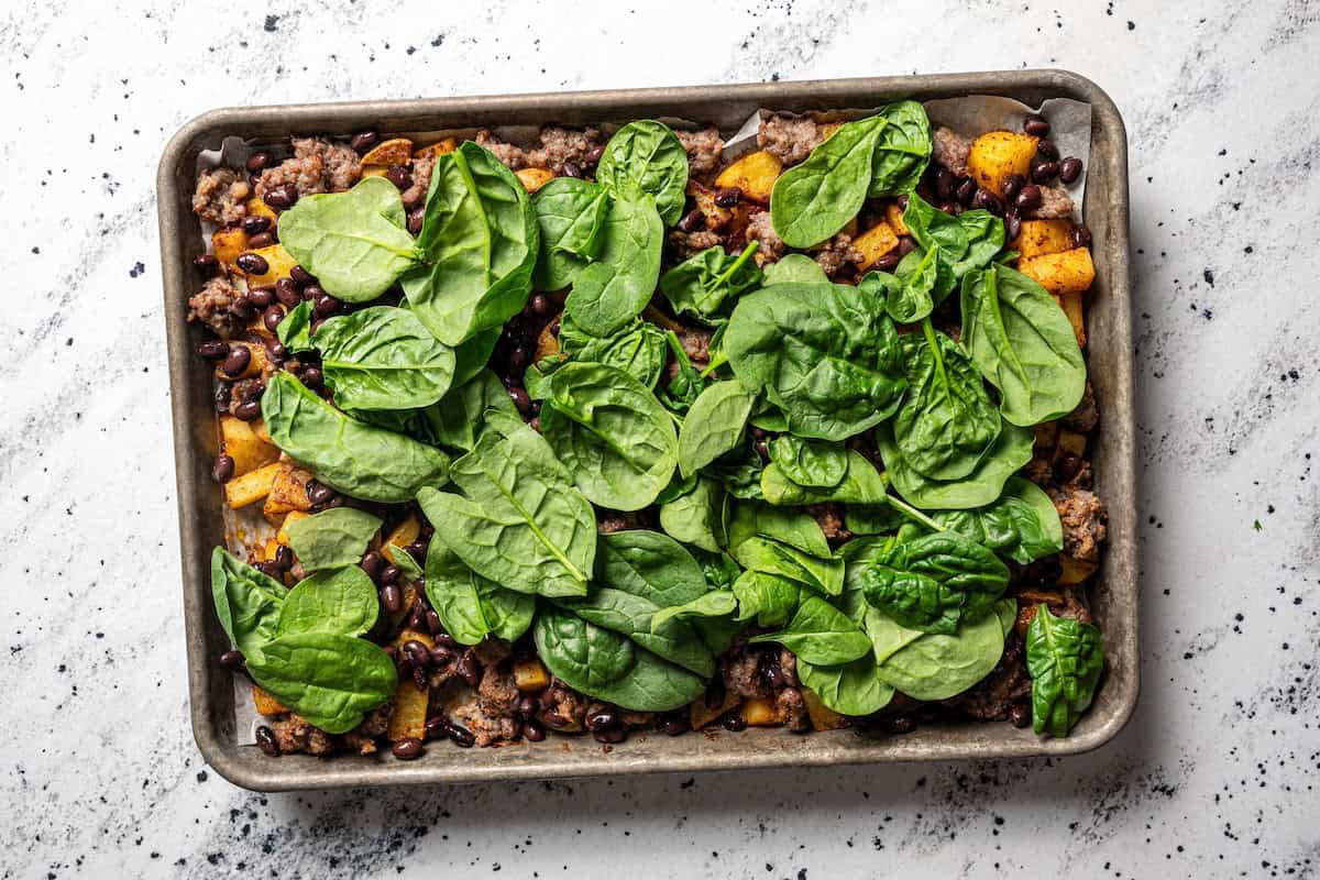 Sheet pan breakfast burritos are an easy way to batch-make breakfast burritos! Bake the filling in one pan, then roll it into soft tortillas. Baby spinach added to a sheet pan with roasted potatoes and sausage.
