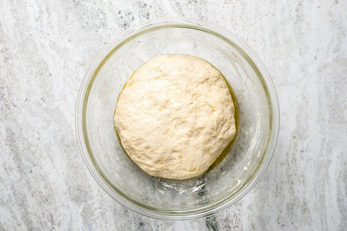 Make this golden, crispy sheet pan pizza recipe with easy homemade dough and your favorite flavorful toppings, like pepperoni and cheese. Risen pizza dough in a glass bowl.