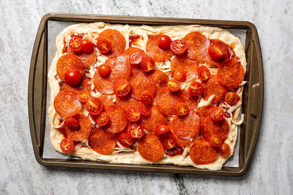 Make this golden, crispy sheet pan pizza recipe with easy homemade dough and your favorite flavorful toppings, like pepperoni and cheese. Toppings added to a sheet pan pizza.