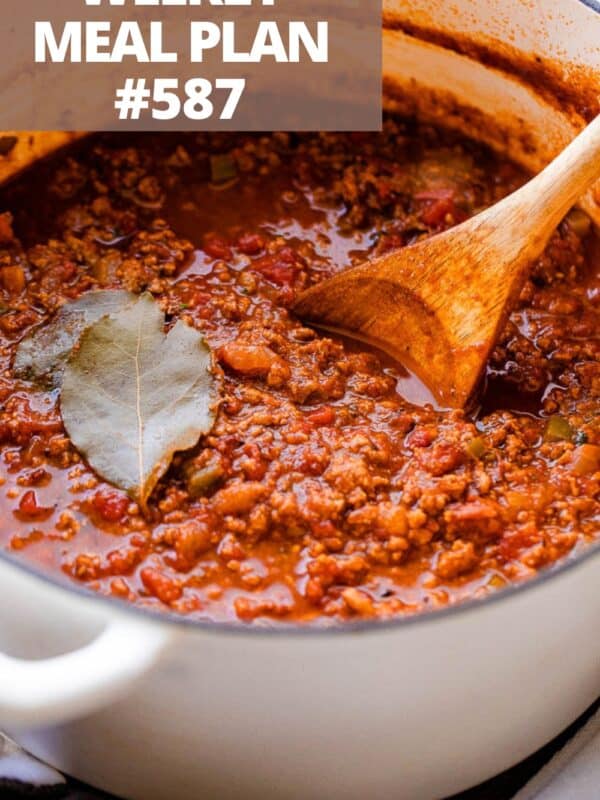 A pot of no-bean chili with ground beef, tomatoes, a bay leaf, and a wooden spoon stirring through it.