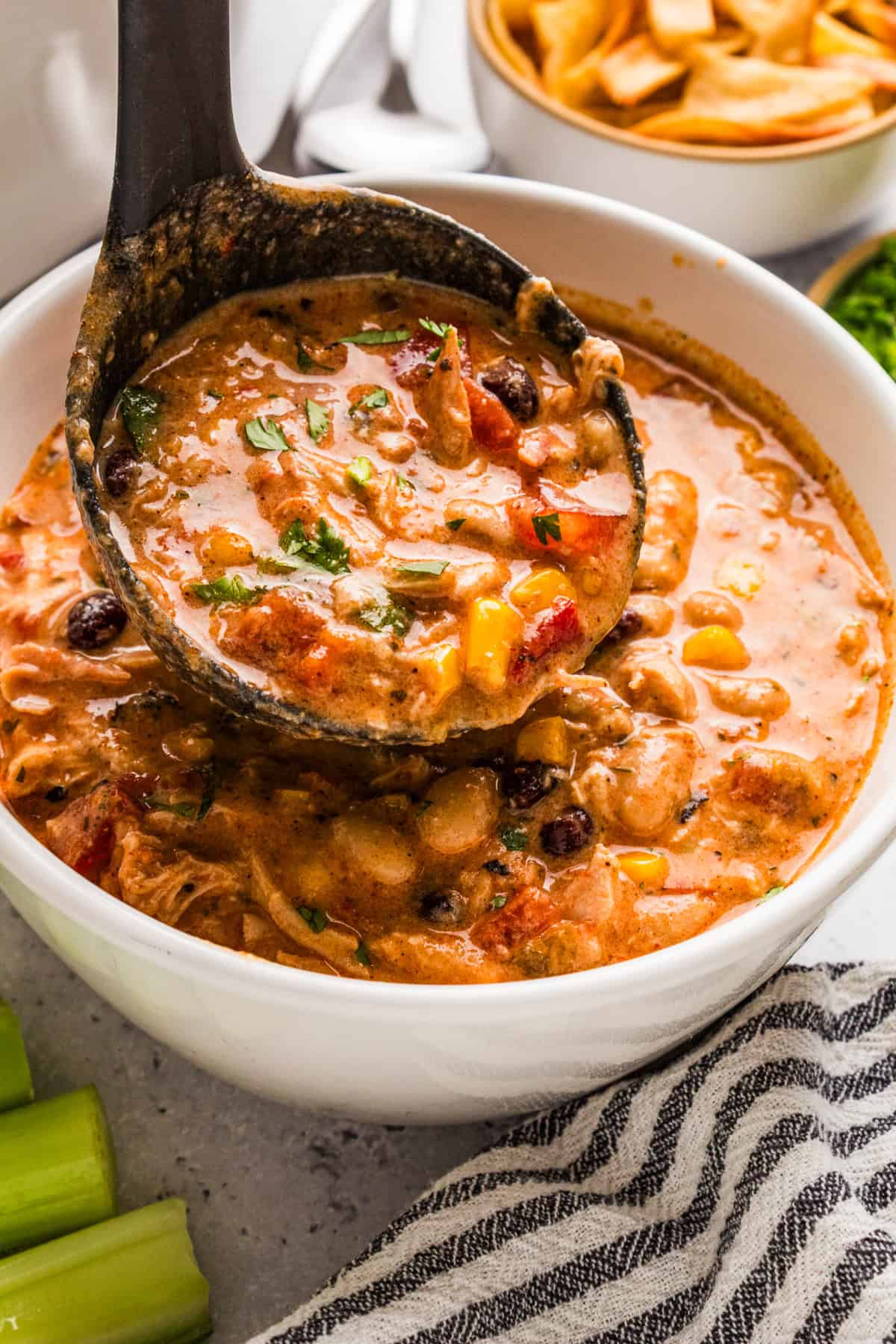 Thick and creamy Buffalo chicken chili prepared with shredded chicken, beans, Buffalo sauce, veggies, and cream cheese. An easy crockpot dinner for weeknights or game day! Slow cooker chicken chili with a ladle scooping up shredded chicken, beans, corn, and creamy Buffalo broth.