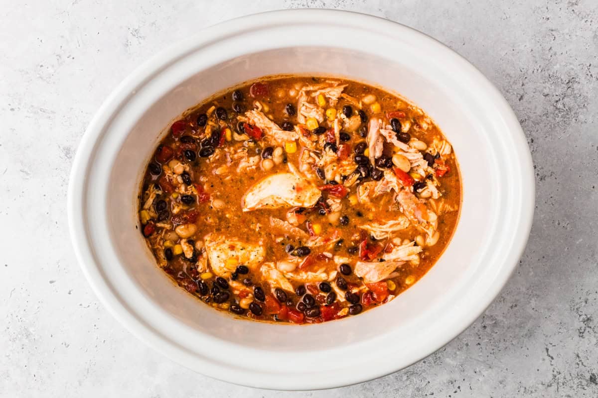 Thick and creamy Buffalo chicken chili made with shredded chicken, beans, Buffalo sauce, and cream cheese. An easy crockpot chili, perfect for weeknights or game day! Crock pot chicken chili with shredded chicken, black beans, white beans, corn, and tomatoes before adding cream cheese.