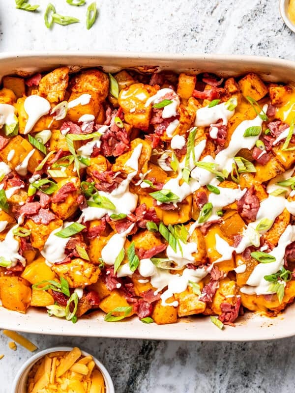 Chicken potato casserole in a baking dish topped with bacon, shredded cheese, green onions, and sour cream.