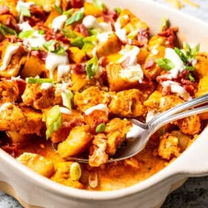 A serving spoon scooping out potatoes from a casserole dish.