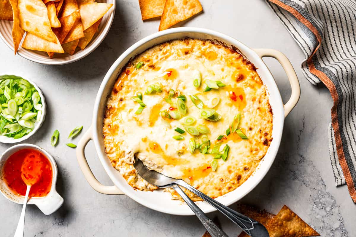 Crab rangoon dip has all those creamy flavors in an easy baked crab dip with cream cheese, sweet chili, green onion, and crispy wonton chips. Baked crab rangoon dip topped with melted cheese, and served with crispy wonton chips.