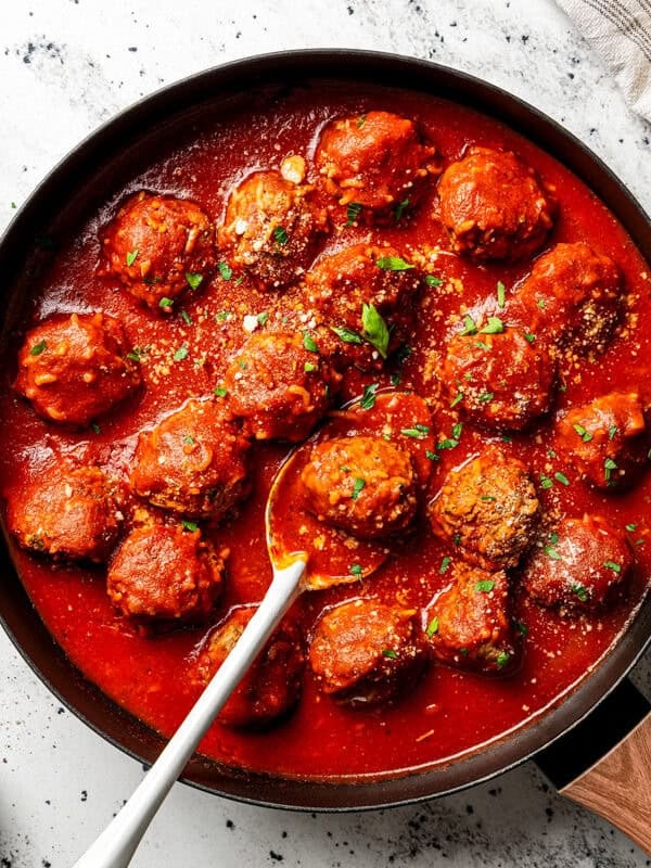 Homemade porcupine meatballs simmering in a tomato sauce in a skillet, garnished with fresh parsley and grated Parmesan cheese.