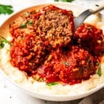 Porcupine meatball cut in half on a fork, showing the tender ground beef and rice filling, served in tomato sauce over creamy mashed potatoes.