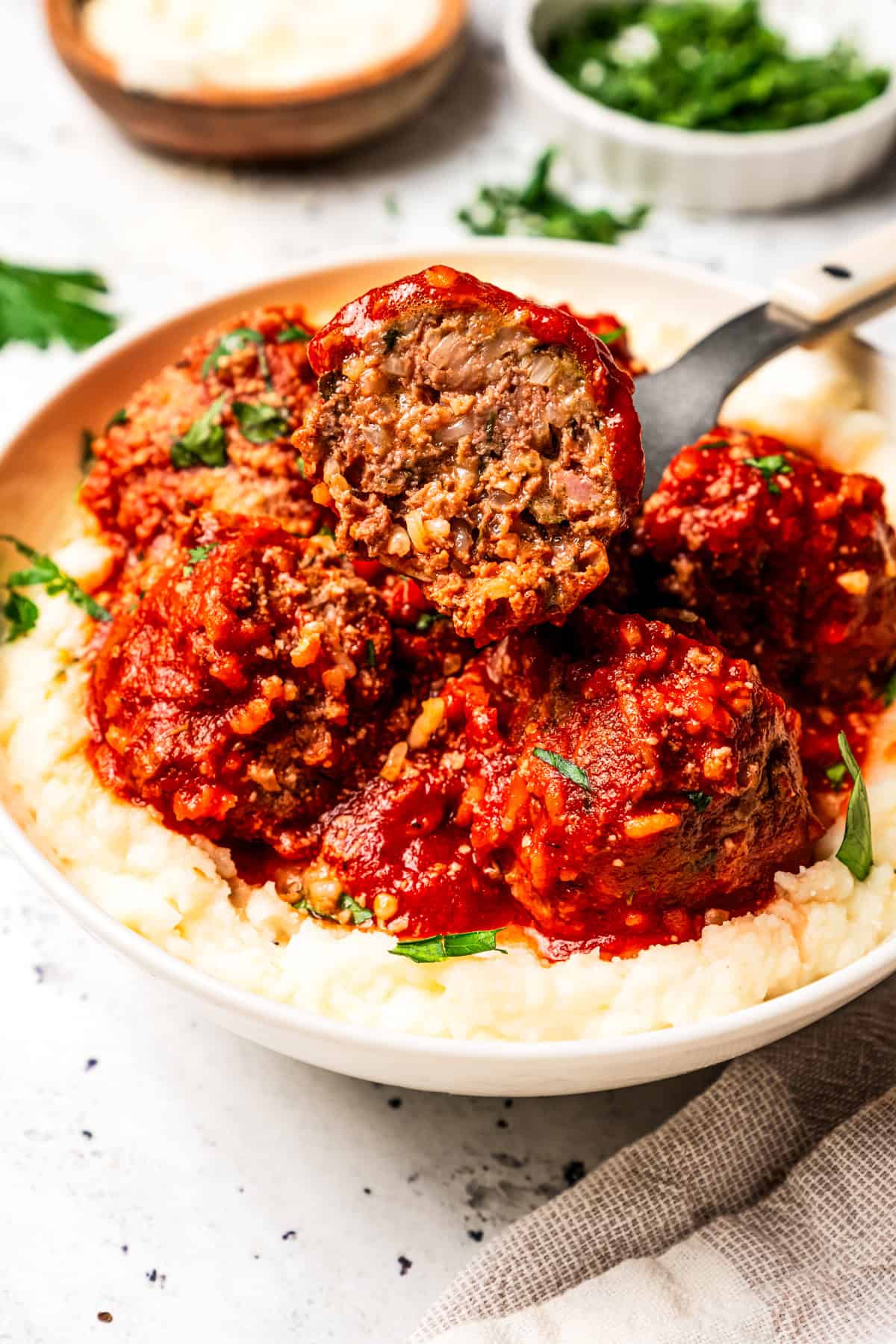 Not your old-fashioned porcupine meatballs! Make these with juicy ground beef, sausage, rice, and herbs, cooked in homemade tomato sauce. Porcupine meatball cut in half on a fork, showing the tender ground beef and rice filling, served in tomato sauce over creamy mashed potatoes.