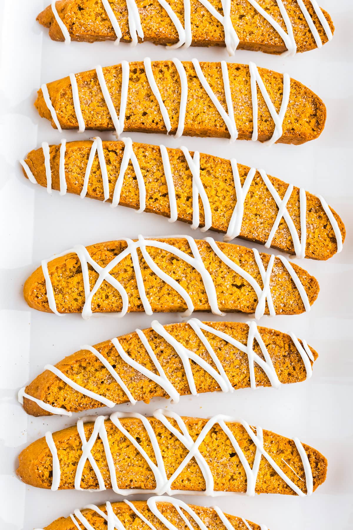 Close-up of crisp pumpkin biscotti topped with cinnamon sugar and white chocolate drizzle.