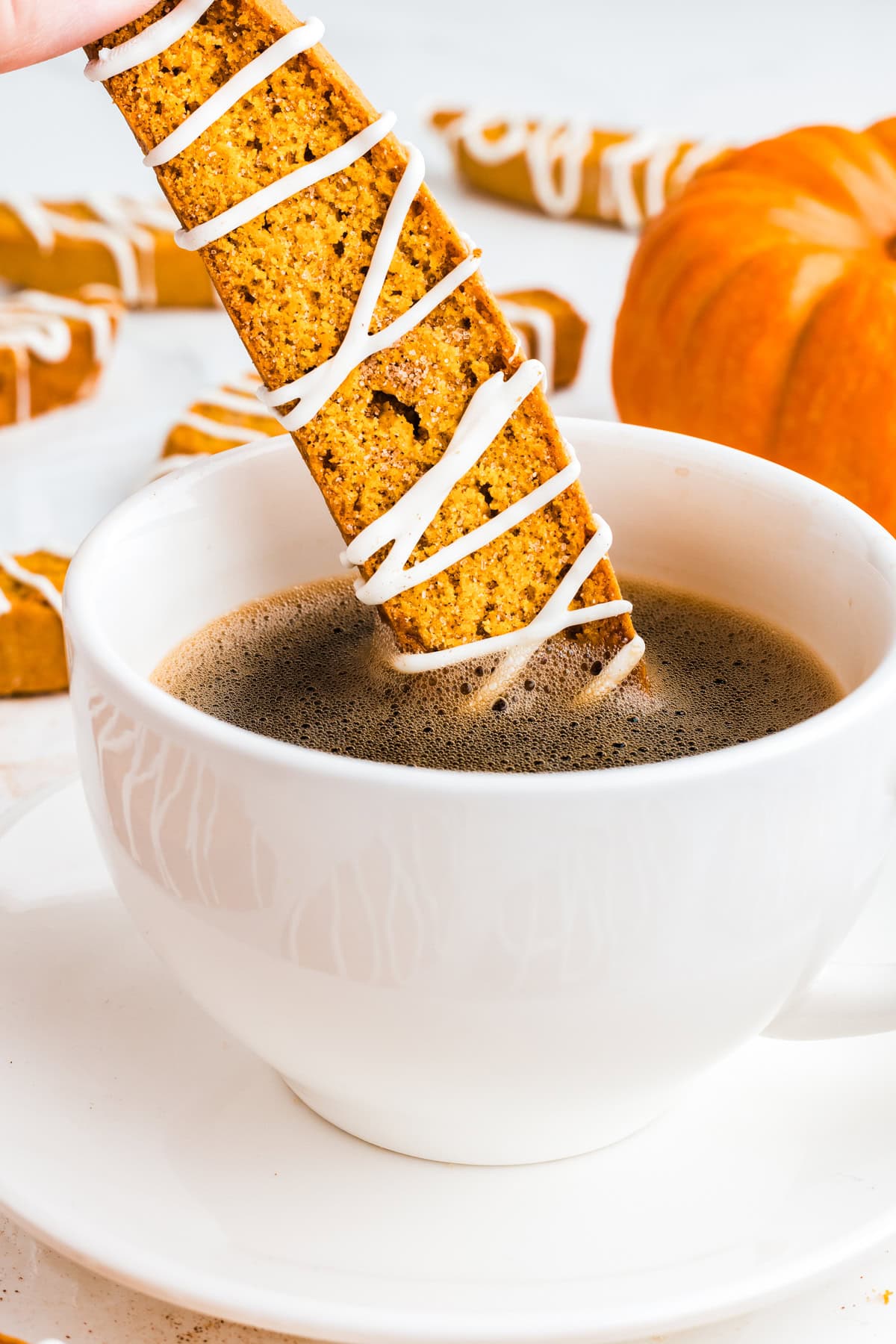 A hand dunking pumpkin spice biscotti in a hot cup of coffee.
