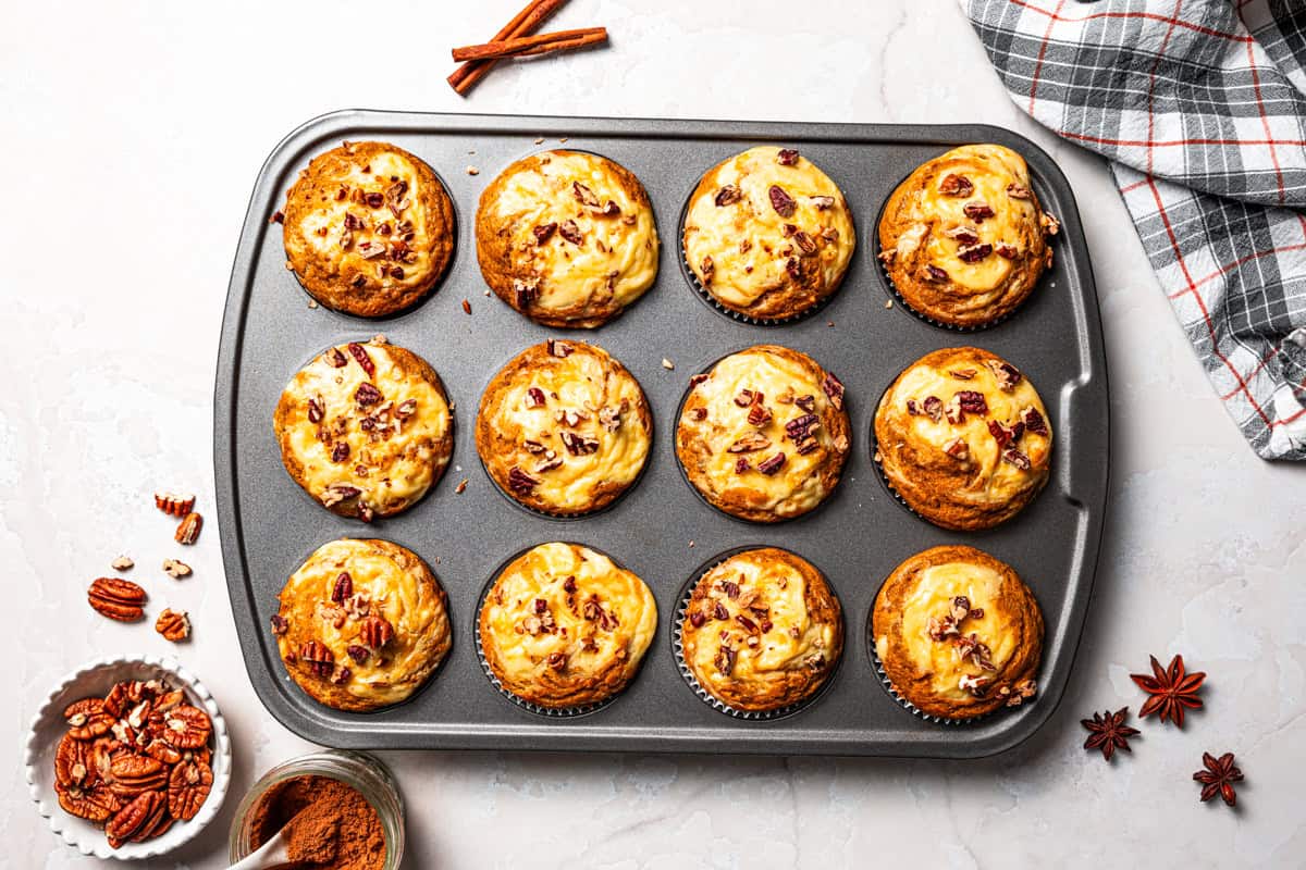 These pumpkin cream cheese muffins are moist, spiced pumpkin muffins swirled with cream cheese filling and topped with toasted pecans. Freshly baked pumpkin cream cheese muffins in a muffin pan.