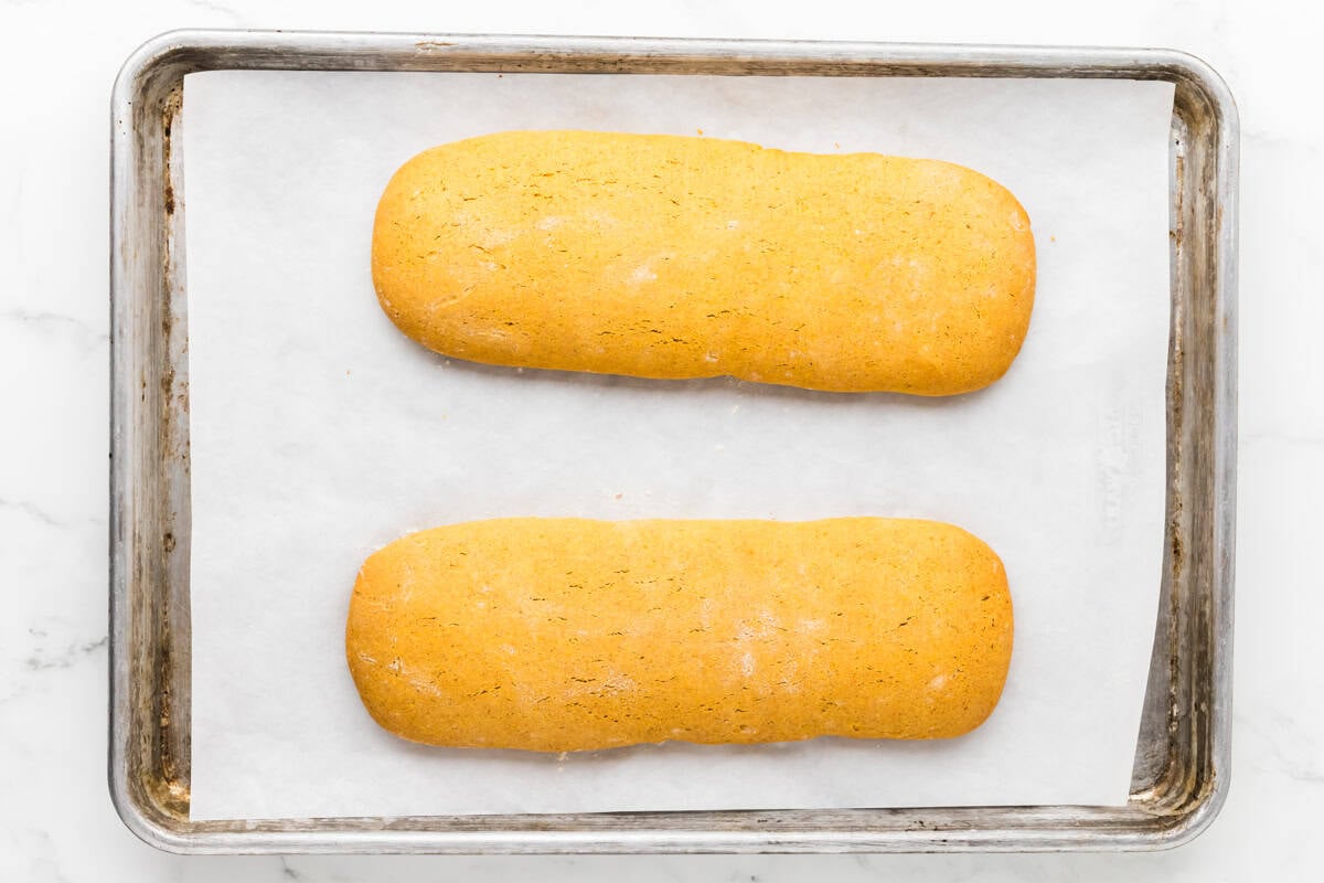 Two baked pumpkin biscotti logs cooling on a parchment-lined baking sheet.