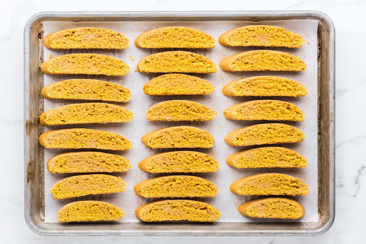 Sliced pumpkin biscotti arranged cut-side up on a baking sheet.