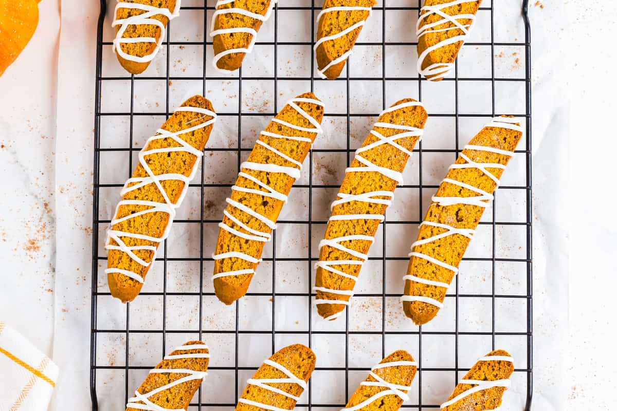 Pumpkin spice biscotti drizzled with white chocolate and arranged on a wire rack.