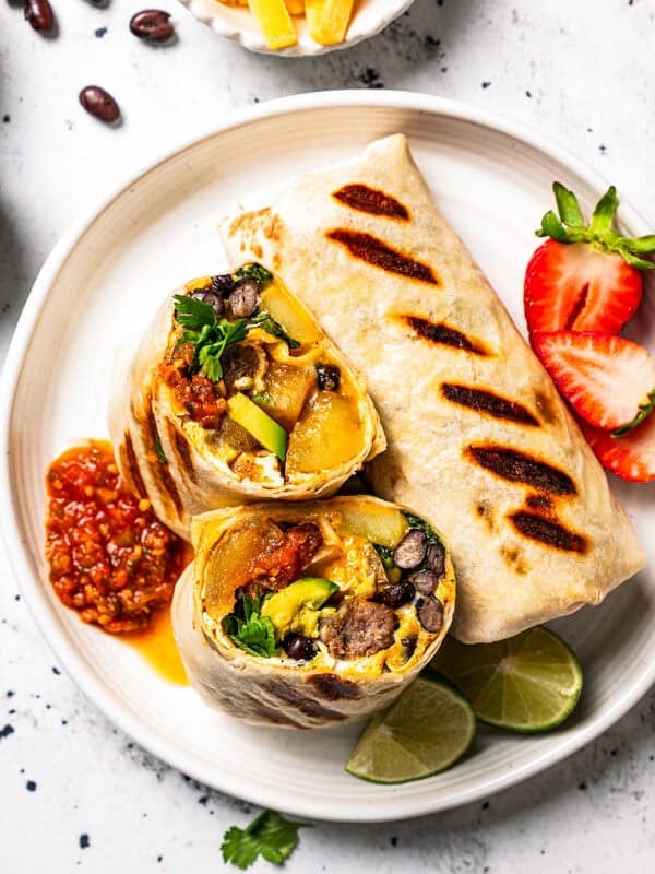 Two sheet-pan-cooked breakfast burritos served on a plate, with one burrito cut in half to show the egg and sausage filling.