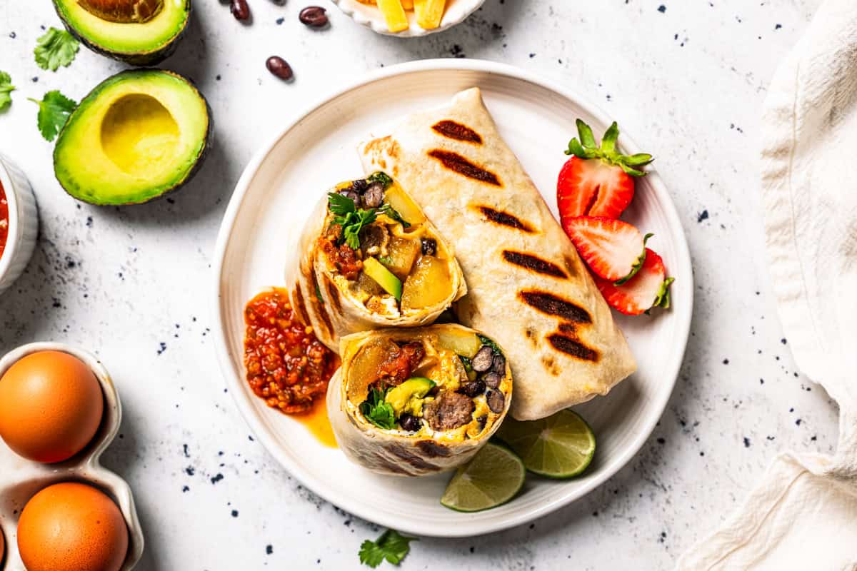 Two sheet-pan-cooked breakfast burritos served on a plate, with one burrito cut in half to show the egg and sausage filling.