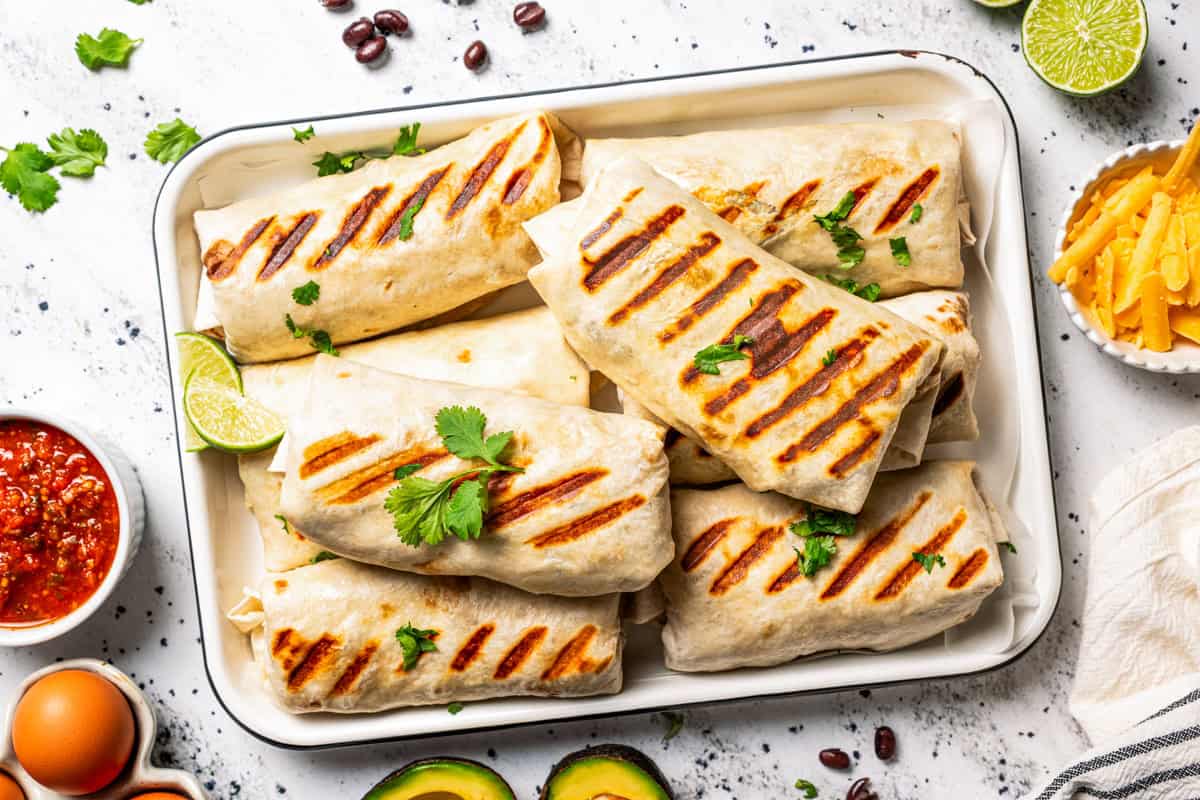 Sheet pan breakfast burritos are an easy way to batch-make breakfast burritos! Bake the filling in one pan, then roll it into soft tortillas. Several breakfast burritos stacked on a tray.