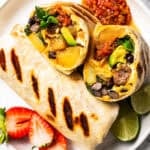 Sheet pan breakfast burritos on a plate, with one burrito cut in half to show the egg and sausage filling.