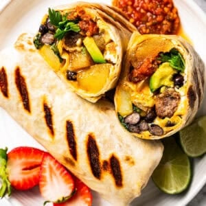 Sheet pan breakfast burritos on a plate, with one burrito cut in half to show the egg and sausage filling.