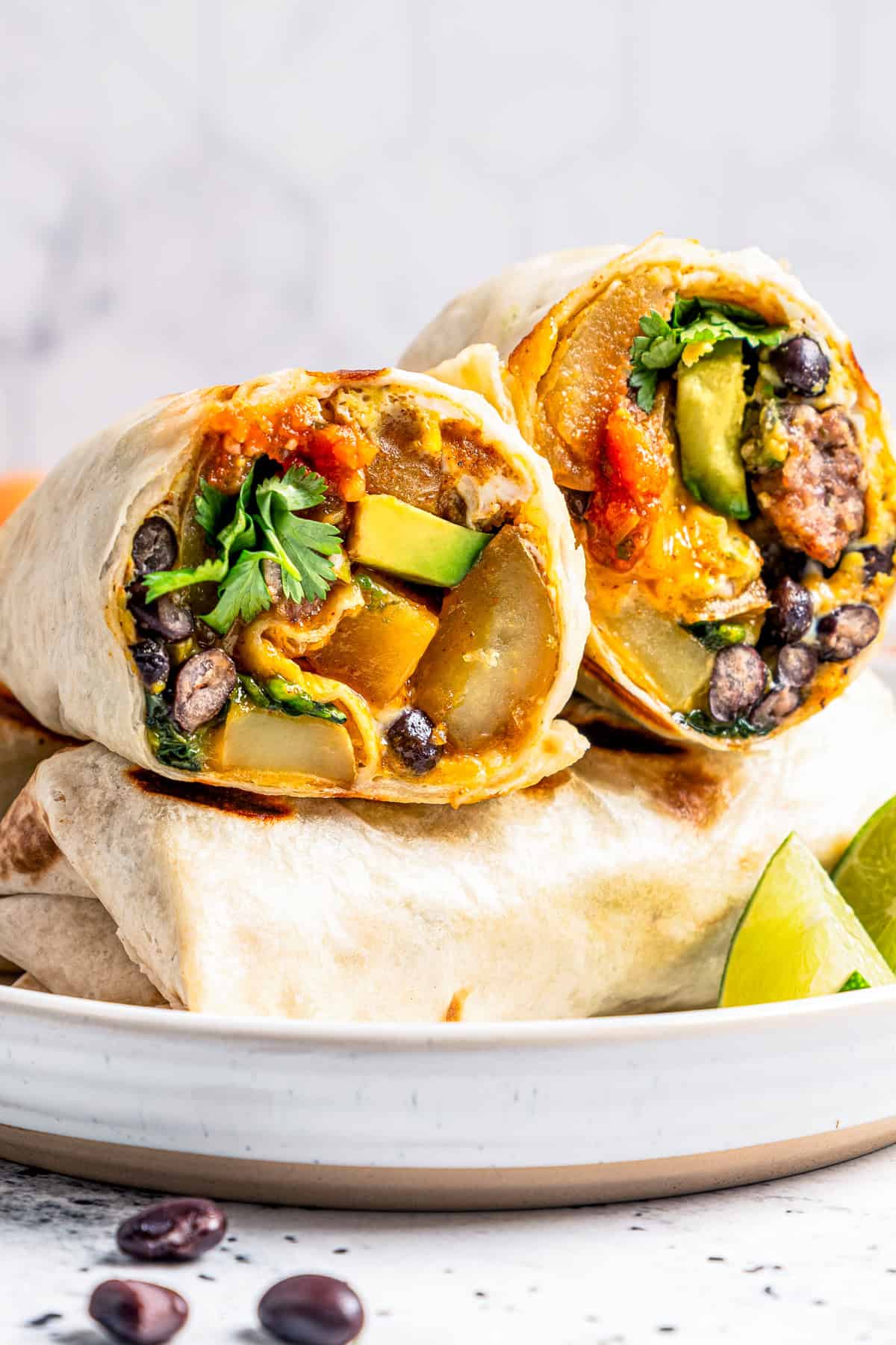 Sheet pan breakfast burritos are an easy way to batch-make breakfast burritos! Bake the filling in one pan, then roll it into soft tortillas. Breakfast burritos stacked on a plate, with one burrito cut in half.