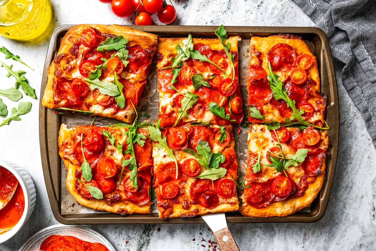 Make this golden, crispy sheet pan pizza recipe with easy homemade dough and your favorite flavorful toppings, like pepperoni and cheese. Sheet pan pizza cut into squares.