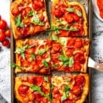 Sheet pan pizza cut into squares and garnished with fresh basil leaves.