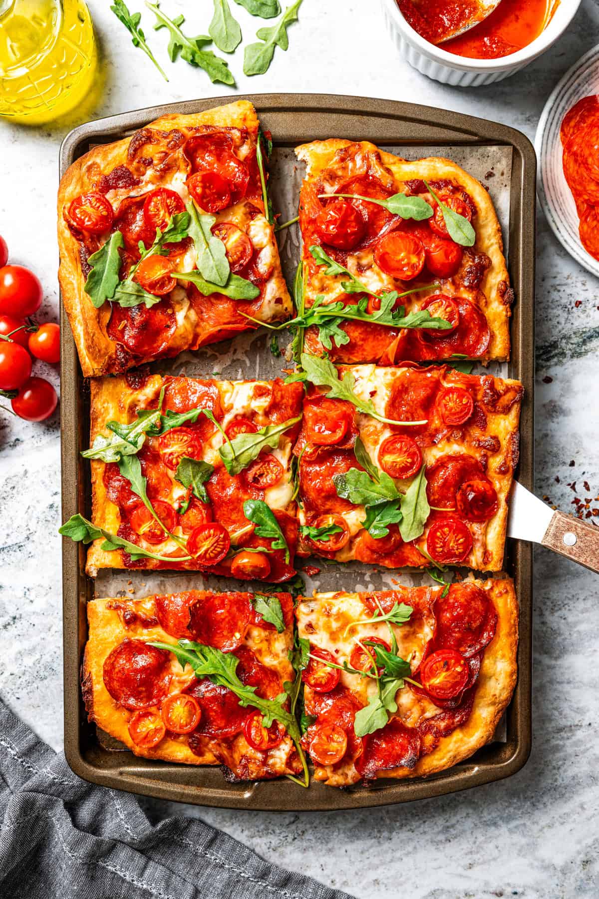 Make this golden, crispy sheet pan pizza recipe with easy homemade dough and your favorite flavorful toppings, like pepperoni and cheese. Sheet pan pizza cut into squares and garnished with fresh basil leaves.